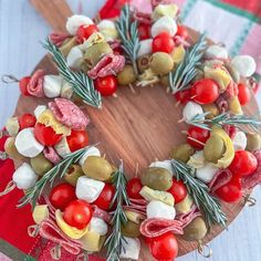 a wreath made out of vegetables and meats on a wooden platter with utensils