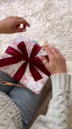 a woman is sitting on the floor holding up a gift box with a red bow