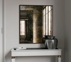 a white table with a mirror and vase on it next to a window in a room