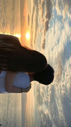 a woman standing in front of the ocean at sunset