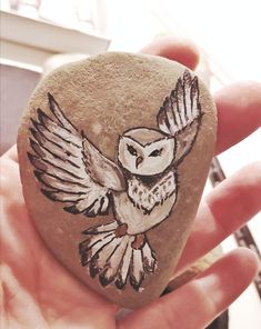 a hand holding a rock with an owl painted on it