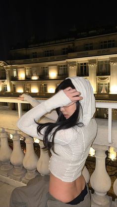 a woman with her hands on her head standing in front of a building at night