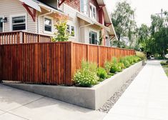 a wooden fence next to a house with plants growing on the top and below it