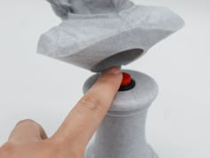 a person touching the top of a gray object with a red button on it's finger