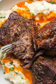 a white plate topped with meat and mashed potatoes covered in gravy next to a fork