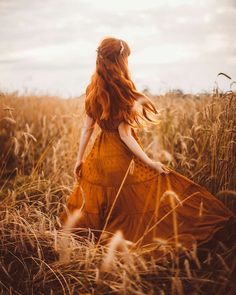 a woman in a yellow dress is walking through tall grass with her hair blowing in the wind