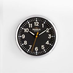 a black and yellow clock on a white wall with the words shinola written below it