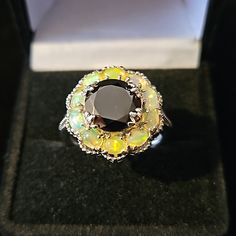 This Elite Shungite And Ethiopian Welo Opal Ring Is Designed With A Flower In Mind The Elite Shungite Ring Has An Adorable Floral Look That Is Beautiful, Elegant, And Will Definitely Have Heads Turned Your Way This Ring Features A Single Round Elite Shungite Gemstone That Is Surrounded By Beautiful Ethiopian Welo Opal Gemstones This Ring Is Crafted In Platinum Over Sterling Silver Shungite Gemstone Is Approx 2.50ctw And Is Appox 10mm In Size There Are 10 Welo Ethiopian Opals That Are Approx 1.25 Black Gemstone Rings For Healing, Black Flower Ring For Wedding, Black Multi-stone Round Rings, Elegant Black Opal Ring Gift, Elegant Black Opal Ring As Gift, Elegant Black Opal Ring For Gift, Black Opal Gemstone Ring, Elite Shungite, Beautiful Ethiopian