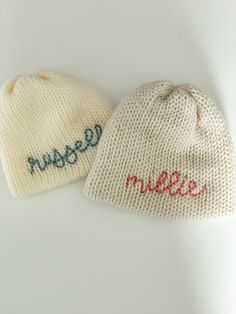 two knitted hats with the word massee written on them, one in red and one in blue