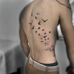 a man's back with birds flying in the sky