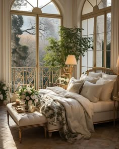 a bed with white sheets and pillows in front of large windows, surrounded by greenery