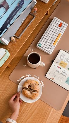 a person sitting at a computer desk with a bagel and coffee in front of them