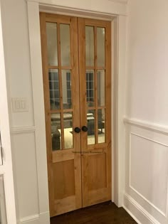 an empty room with two wooden doors and hard wood flooring on the side walk