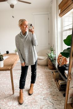 an older woman taking a selfie in her living room while wearing jeans and sweater