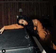 a woman laying on top of a black suitcase next to a lamp and wooden wall