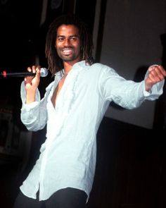 a man with dreadlocks holding a microphone in one hand and smiling at the camera