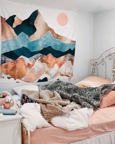 an unmade bed with pillows and blankets on it in front of a wall hanging