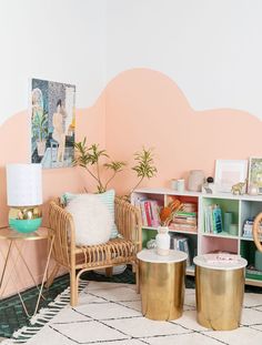 a living room filled with furniture and a pink painted wall behind the chair is a gold side table