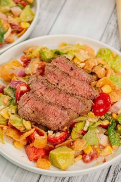 a steak salad on a white plate with corn, tomatoes, and avocado