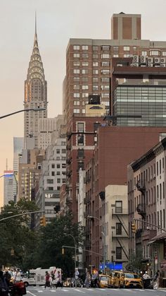 a city street filled with lots of tall buildings next to traffic and people walking on the sidewalk