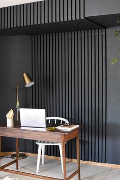 a desk with a laptop on it in front of a black wall and white rug