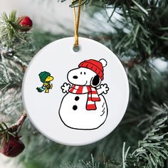 a white ornament with a cartoon snowman on it hanging from a christmas tree