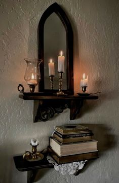 some books and candles are sitting on a shelf in front of a mirror that is hanging from the wall