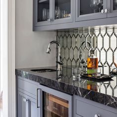 a kitchen with gray cabinets and marble counter tops, wine glasses on the cabinet doors