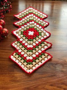 two crocheted christmas tree ornaments on a wooden table next to red and green ornaments