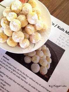 a white bowl filled with powdered sugar covered donuts on top of a table