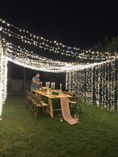 a man standing next to a table with candles on it in the middle of a field