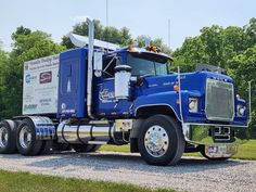 a large blue semi truck parked on the side of a road next to some trees