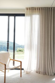 a white chair sitting in front of a window with sheer curtains on top of it