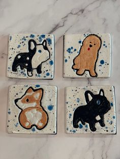 four ceramic coasters with dogs on them sitting on a marble counter top, each decorated in different colors and shapes