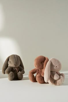 three stuffed animals sitting next to each other on a white surface with a light in the background