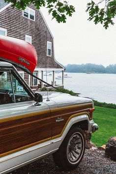 an old car with a canoe on top parked in front of a house near the water