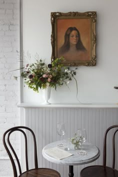 two chairs and a table in front of a painting on the wall with flowers next to it