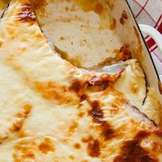 a cheesy pizza in a white dish on a red and white checkered table cloth