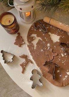 cookie cutters and cookies on a table next to a lit candle, christmas tree ornament