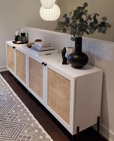 a vase with some plants on top of it next to a white cabinet and rug