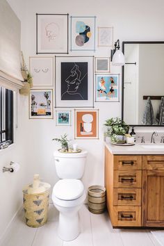 a white toilet sitting next to a wooden cabinet in a bathroom with pictures on the wall