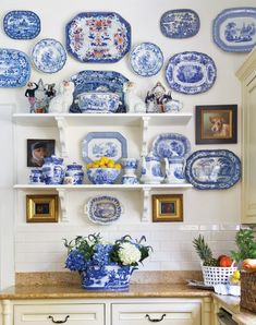 blue and white plates are hanging on the wall above a kitchen countertop with flowers in vases