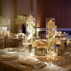 the table is set with candles and flowers in tall glass vases on each side