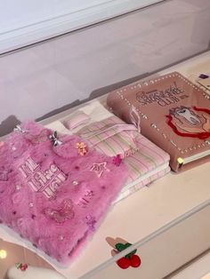 there is a pink blanket on top of a white table next to a book and other items