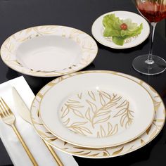 the table is set with white and gold plates, silverware, and wine glasses