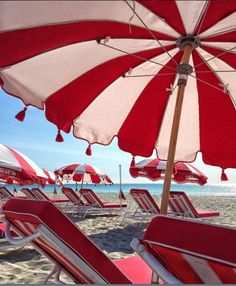 red and white beach chairs under umbrellas on the beach