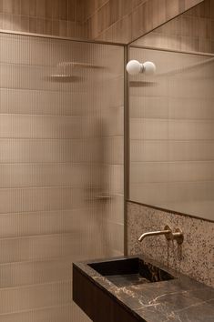 a bathroom sink sitting under a mirror next to a walk in shower and tiled walls