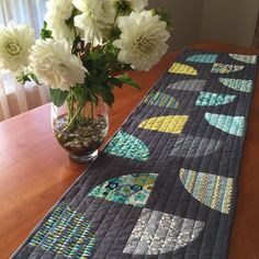 a vase filled with white flowers sitting on top of a wooden table next to a quilted runner