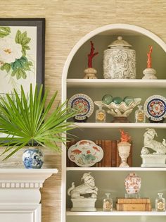 a white book shelf with plates and vases on it next to a potted plant