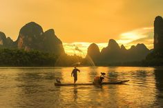 two people on a boat in the water with mountains in the backgrouds